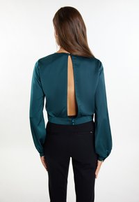 Tegenlichte satijnen blouse met lange mouwen, een opening met sleutelgat aan de achterkant en een knoopsluiting in de nek. Gecombineerd met zwarte stijlvolle broek.