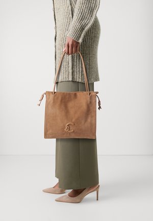 Brun suede håndveske med lærhåndtak, rektangulært design, preget logo og snor detaljer. Kombinert med olivenfargede bukser og nude hæler.