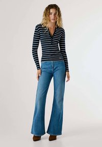 Marinblå randig långärmad topp med henley-hals, kombinerad med utsvängda blå jeans och bruna ankelboots. Outfiten har en avslappnad passform och design.