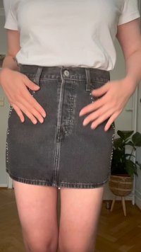 Črna denimska mini krilo s prilagojenim dizajnom, ki ima srebrne nabarvane detajle ob straneh in sprednje zaklepanje na gumb.