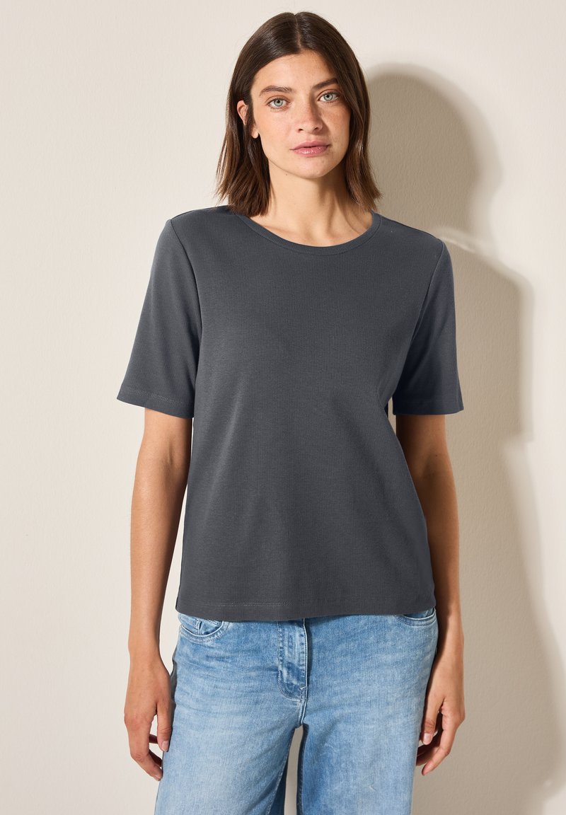 Grå, kortærmet t-shirt med rund halsudskæring og ribbet struktur, parret med lysblå denim jeans. Simpelt design, ingen synlige mønstre.