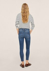 Jeans ajustados en denim azul medio, con una cintura alta y bolsillos traseros, combinados con una camisa de manga larga de rayas blancas y negras y zapatos marrones.