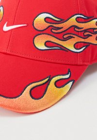 Κόκκινο καπέλο από ύφασμα με κεντημένα κίτρινα και πορτοκαλί γραφικά φλόγας και λευκό λογότυπο Nike στο μπροστινό πάνελ.
