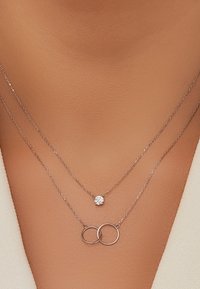 Silver necklace featuring two layers: one with a round crystal pendant and another with interlinked circular charms.