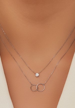 Collier en argent à deux couches : une avec un pendentif en crystal rond et une autre avec des charms circulaires entrelacés.
