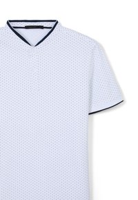 Polo shirt bianco a maniche corte con colletto henley, caratterizzato da rifiniture blu navy e piccoli pois neri distribuiti su tutta la stoffa.