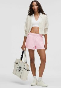 Light pink shorts with an elastic waistband, paired with a white crop top and a cream open-knit cardigan. Accessories include a beige tote bag.