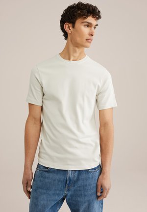 Tricou scurt din bumbac neted, de culoare bej deschis, cu guler rotund, croială lejeră, asortat cu blugi din denim albastri. Design simplu și minimalist.
