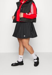 Czarna plisowana spódnica z białym logo, czerwona skrócona bluza z kapturem oraz czarna kamizelka puchowa. Uzupełnione białymi skarpetkami i czarnymi butami na klamrę.