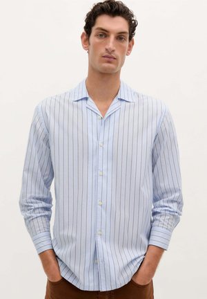 Camisa de botones azul claro con rayas verticales, de mangas largas y con collar. Presenta un dobladillo recto y una textura de tela suave.