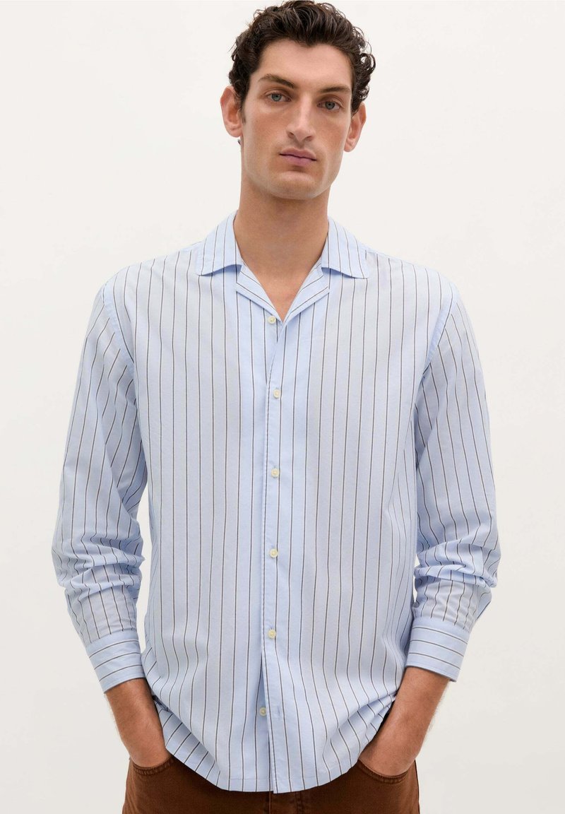 Camisa de botones azul claro con rayas verticales, de mangas largas y con collar. Presenta un dobladillo recto y una textura de tela suave.