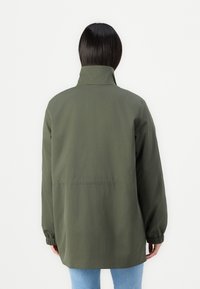Veste vert olive avec un col haut, des manches longues et des poignets élastiques ; présente une coupe décontractée et une texture lisse. Vue arrière montrée.
