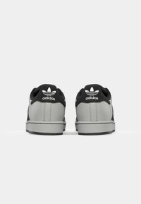Black and gray Adidas sneakers feature a smooth upper with textured accents, padded collar, and a white logo on the heel. Flat rubber sole.
