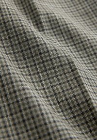 Textured fabric featuring a plaid pattern in dark green and black tones, with subtle interwoven threads creating depth and dimension.