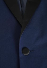 Giacca da abito blu navy con rever in satin nero, chiusura con un bottone nero e tessuto morbido con una leggera lucentezza.