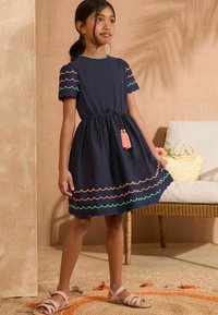 Rochie din bumbac bleumarin cu mâneci scurte, margine ondulată în roz, verde și portocaliu, talie strânsă și detaliu cu ciucuri în față.