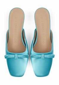 Mules en satin turquoise à enfiler, avec une semelle plate, un bout carré et un détail en nœud à l'avant, offrant une texture lisse et une semelle intérieure beige.