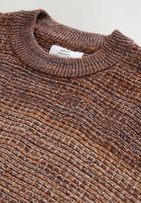 Sweter dziergany w brązowych i niebieskich tonacjach, z teksturowanym, szachownicowym wzorem, prążkowanym okrągłym dekoltem oraz metką wskazującą regularny krój.