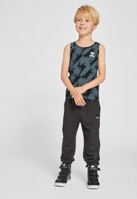 Zwart en teal tanktop met zigzagpatroon, gecombineerd met zwarte joggers. Zwarte hoge sneakers maken de outfit compleet.