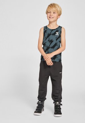 Czarny i zielonkawo-niebieski top na ramiączkach z zygzakowatym wzorem, zestawiony z czarnymi dresami. Całość dopełniają czarne sneakersy za kostkę.