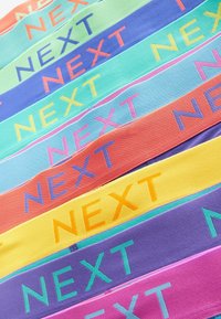 Színes szövetcsíkok, amelyeken a "NEXT" szó kontrasztos színekben van nyomtatva. Különböző árnyalatú kék, zöld, narancs, lila és sárga színek találhatóak.