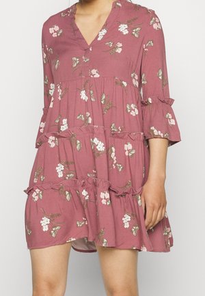 Mauve tiered dress with pink and white floral and butterfly print, V-neck, and three-quarter ruffled sleeves on a standing person.