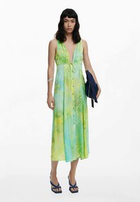 Maxikleid im grünen und blauen Ombre-Muster, tiefer V-Ausschnitt, Taillenschleife, Knopfleiste vorne, kombiniert mit einer marineblauen Clutch und Plateausandalen.