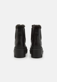 Botas de tobillo de cuero negro con un cuello de piel sintética, costados texturizados y una suela gruesa negra. Cuenta con paneles laterales elásticos y marca.