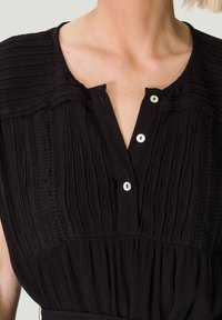 Robe noire texturée avec des plis verticaux, fermeture à boutons et détails froncés aux épaules. Tissu doux, manches courtes et col.