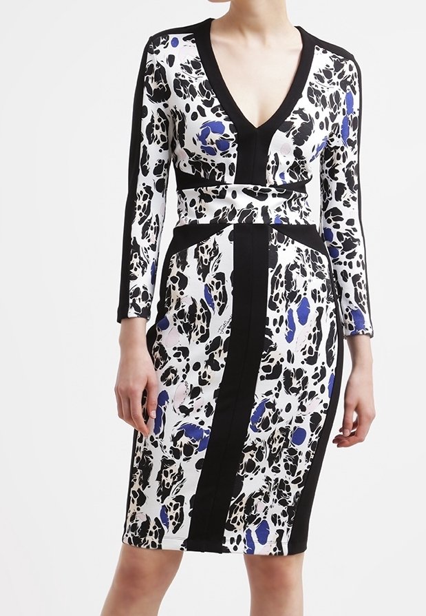 Femme portant une robe ajustée avec un motif abstrait noir, blanc et bleu, un profond décolleté en V, des manches longues et des rayures noires verticales.