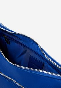 Blaue Ledertasche mit Innentaschen und Reißverschlüssen, die über eine glatte Textur verfügt und ein kleines Etikett im Futter hat. Das Hauptfach ist geräumig.