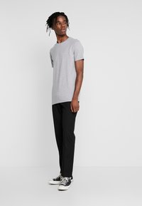 Szara koszulka z krótkim rękawem, czarne spodnie slim-fit i czarne sneakersy niskie z białą podeszwą. Proste faktury i minimalistyczny design.