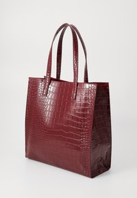 Sac fourre-tout bordeaux brillant avec un motif crocodile. Dispose de deux poignées robustes et d'une forme rectangulaire structurée avec un fond plat.