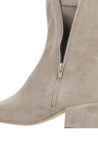 Beiger Wildleder-Stiefelette mit seitlichem Reißverschluss und Blockabsatz, der Reißverschluss teilweise geöffnet und detaillierte Nähte sichtbar.