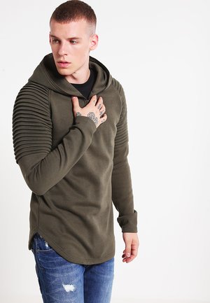 Olivenfarvet hætte sweatshirt med ribbede skulderdetaljer, lange ærmer og en buet kant. Båret med slidte blå jeans.
