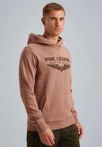 Sweat-shirt à capuche de couleur brun clair, fabriqué en tissu doux, comportant une poche avant et un logo imprimé avec un motif d'ailes sur la poitrine.