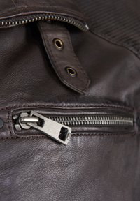 Bruine leren tas met een opvallende zilveren rits, decoratieve stiksels en een drukknoopsluiting met goudkleurige accenten.