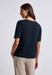 Haut à manches courtes bleu marine avec un décolleté large, texture lisse et coupe décontractée, associé à un pantalon beige avec des rayures sur les côtés.