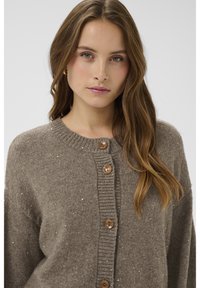 Rudas tekstūruotas megztinis su ribbingo apykakle, sagų užsegimu ir subtiliais žėrinčiais akcentais visame audinyje.