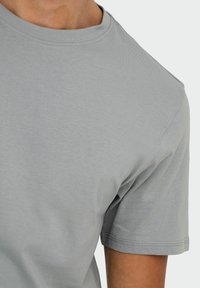 Camiseta gris de manga corta hecha de una tela suave y ligera. Presenta un cuello redondo y detalles de costura sutiles a lo largo del dobladillo y las mangas.