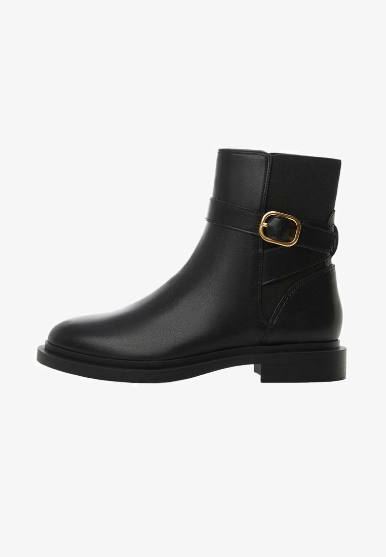Botte cheville en cuir noir avec bout arrondi, semelle plate, et une bride latérale ornée d'une boucle dorée. Texture lisse et design minimaliste.