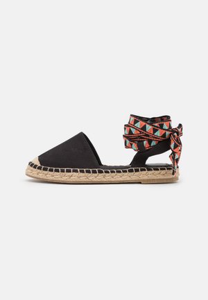 Sandale espadrille noire avec semelle tressée couleur tan et liens à la cheville à motifs géométriques colorés en bleu, orange et noir.