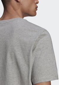 Maglietta grigia a maniche corte con una texture morbida in cotone, caratterizzata da un collo tondo e un design semplice, vista da dietro.