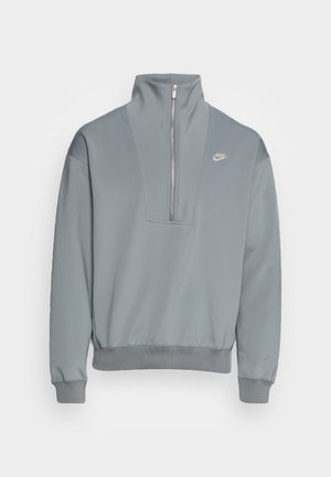 Maglione Nike grigio chiaro con collo alto e zip frontale a metà, polsini e orlo a costine, e piccolo logo Nike sul petto a sinistra.