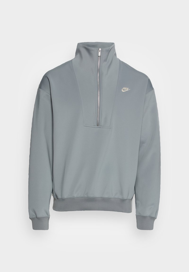 Sudadera gris claro de Nike con cuello alto y media cremallera frontal, puños y dobladillo acanalados, y pequeño logo de Nike en el pecho izquierdo.