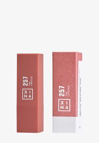 Leppestift i en matt ferskenfarge, merket "257 THE LIPSTICK," sammen med sin rosa eske med hvit tekst som gir produktinformasjon.