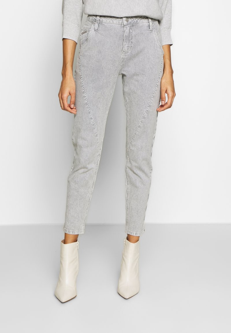 Pantaloni a strisce, svasati, realizzati in tessuto leggero, con vita alta e tasche laterali, abbinati a stivali beige a tacco, alte alla caviglia.