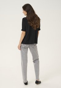 Schwarze Bluse mit kurzen Ärmeln und Rüschensaum, kombiniert mit hochtaillierten hellgrauen Jeans mit dekorativer Naht und geradem Bein.