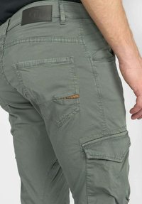 Groene cargobroek met een achterzak voorzien van een decoratieve strook, textuurstof en een leren patch op de tailleband.