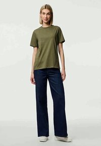 T-shirt de algodão verde-azeitona com gola redonda, combinado com jeans de perna larga azul-escuro. A textura é suave e o ajuste é casual.